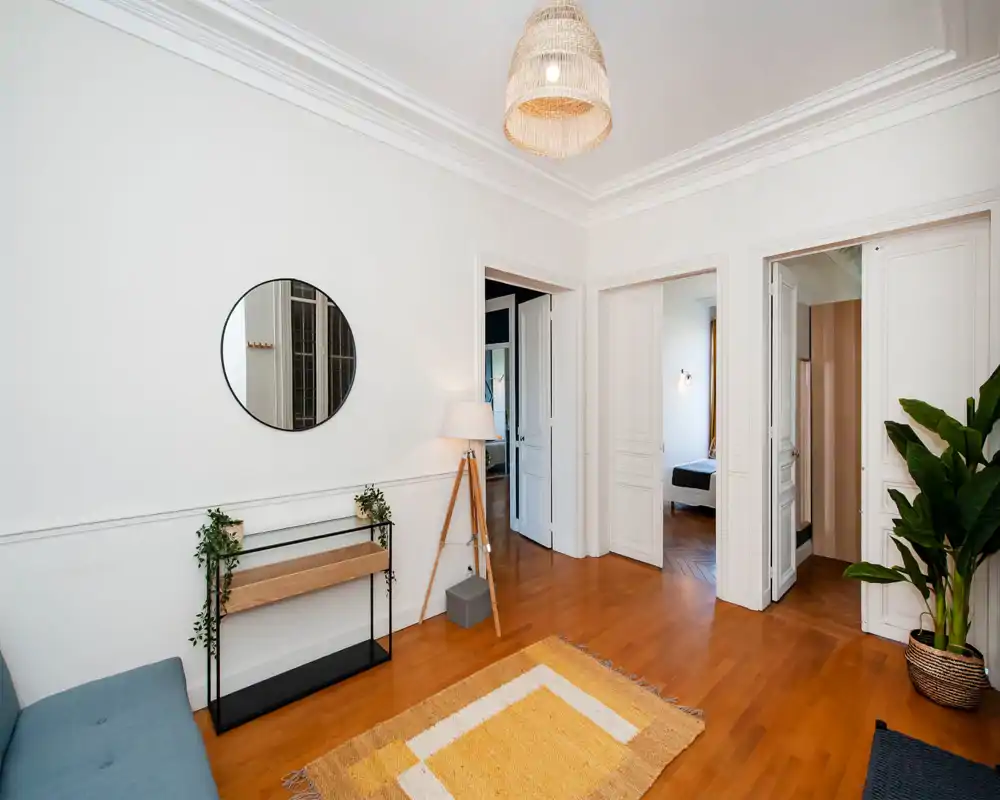 Espace de vie lumineux et élégant avec parquet chaleureux, suspension tressée, tapis décoratif et plantes, créant une ambiance calme et accueillante.