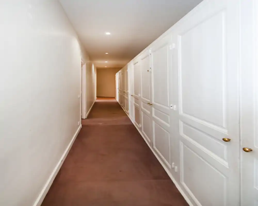 Couloir intérieur étroit avec placards blancs intégrés et spots encastrés au plafond, offrant beaucoup de rangement le long du passage.