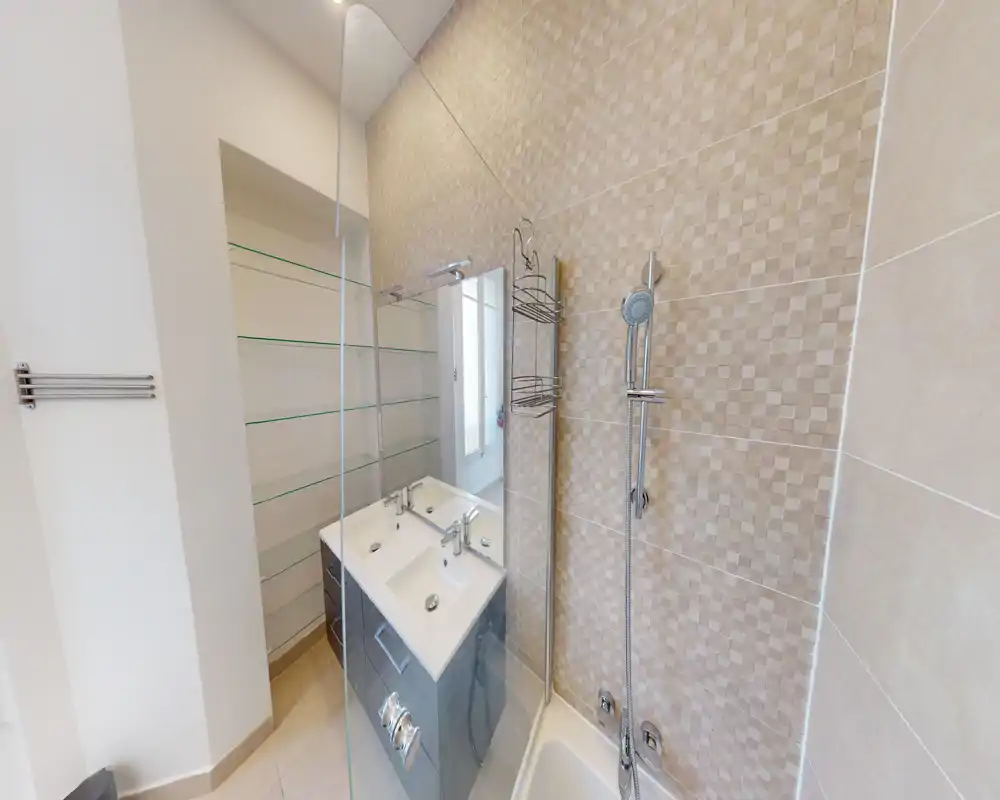 Salle de bain moderne avec meuble lavabo double, paroi de douche en verre et douche murale ; carreaux beige neutre et robinetterie chrome pour un rendu propre et contemporain.