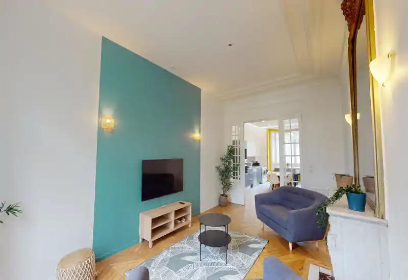 Salon lumineux et stylé avec un mur d'accent bleu-vert, TV murale, canapés confortables, plantes et tapis à motifs — clair et bien mis en scène.