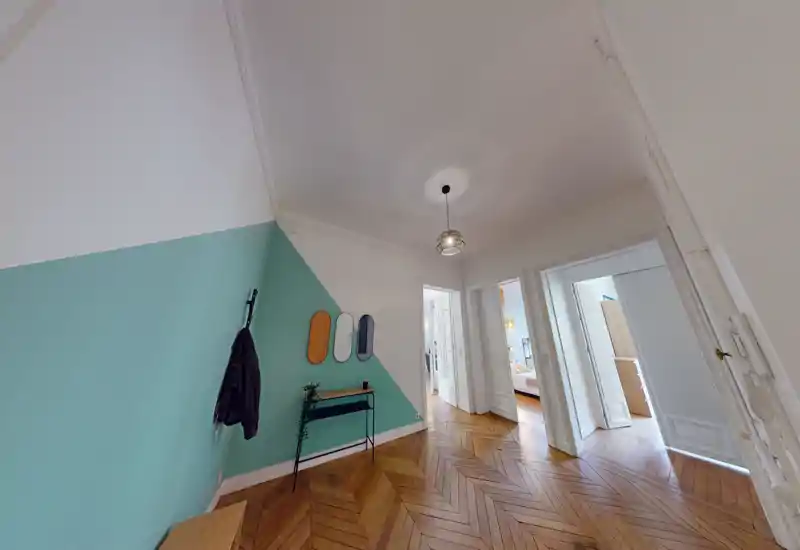 Entrée spacieuse et lumineuse avec mur d'accent bleu-vert, patères murales et parquet en chevrons menant aux pièces adjacentes.