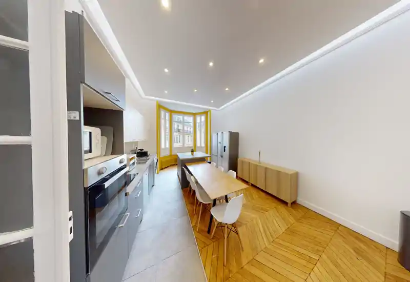 Cuisine moderne et lumineuse en open-space avec électroménagers intégrés, longue table à manger et grande baie vitrée apportant beaucoup de lumière naturelle.