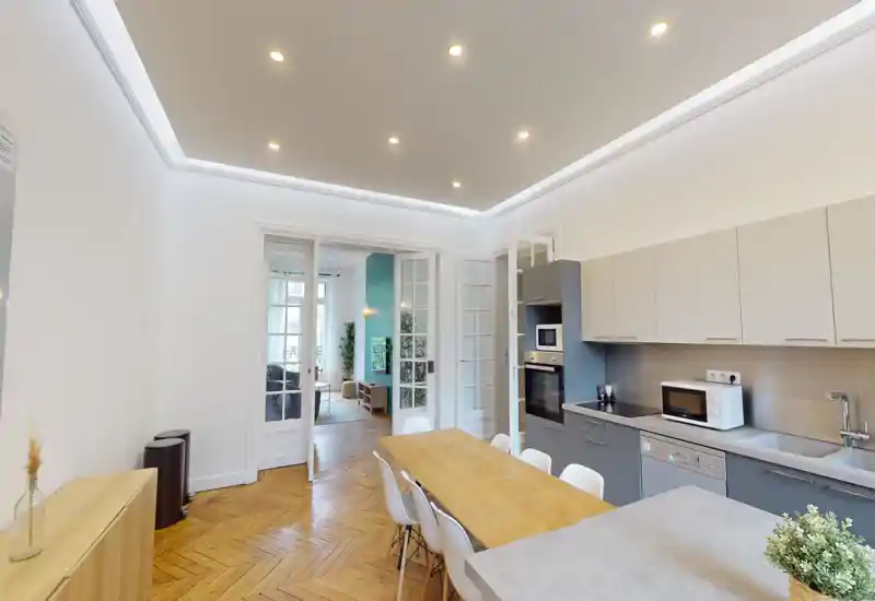 Cuisine moderne équipée avec table à manger intégrée, rangements clairs, four et micro-ondes encastrés et parquet chaleureux; espace lumineux et accueillant pour cuisiner et dîner.
