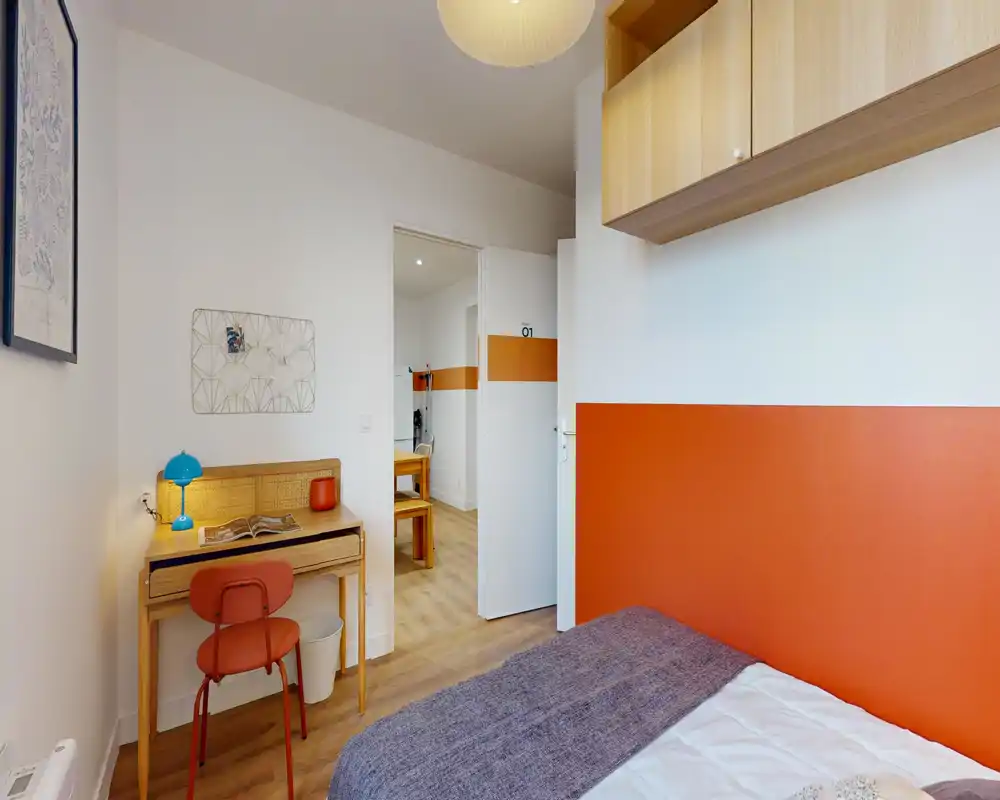 Compact, well-lit bedroom with a single bed dressed in neutral linens, a small wooden desk and colorful accents that create a warm, functional space ideal for a student or solo traveler.