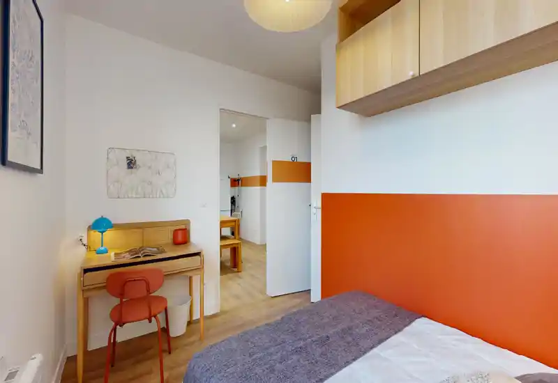 Compact, well-lit bedroom with a single bed dressed in neutral linens, a small wooden desk and colorful accents that create a warm, functional space ideal for a student or solo traveler.