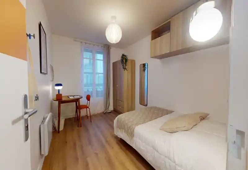 Compact, well-lit single bedroom with a comfortable bed, wooden wardrobe, small desk and warm wood flooring — ideal for a student or solo professional.