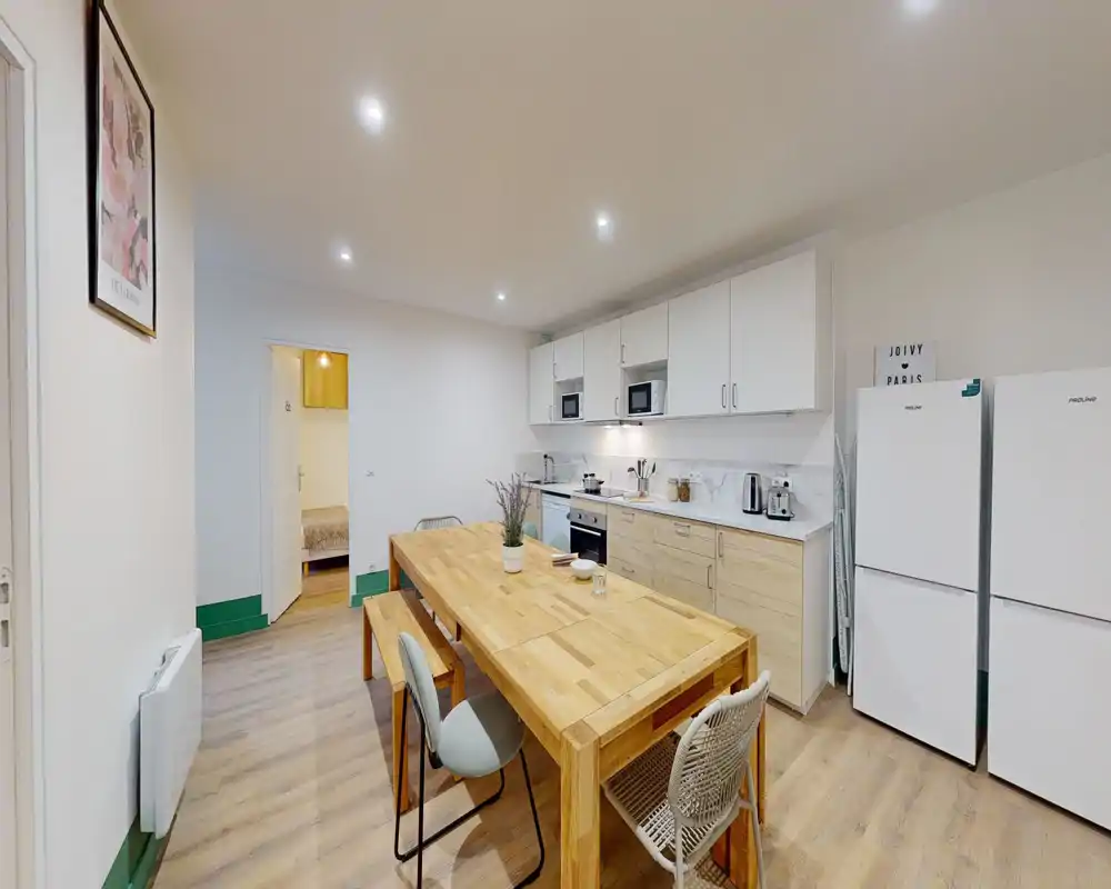 Cuisine moderne et lumineuse avec grande table en bois, meubles intégrés, électroménagers et deux frigos — idéale pour colocation.