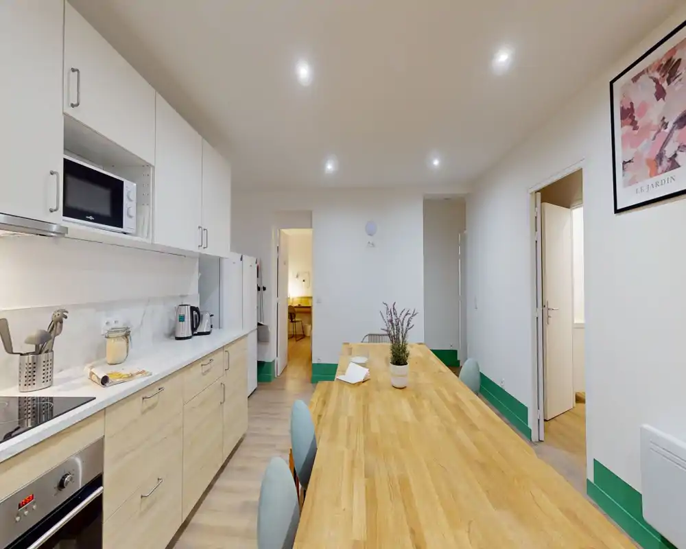Cuisine moderne ouverte avec une longue table en bois, placards clairs, électroménagers intégrés et éclairage encastré lumineux — idéale pour des repas conviviaux et une cuisine légère.