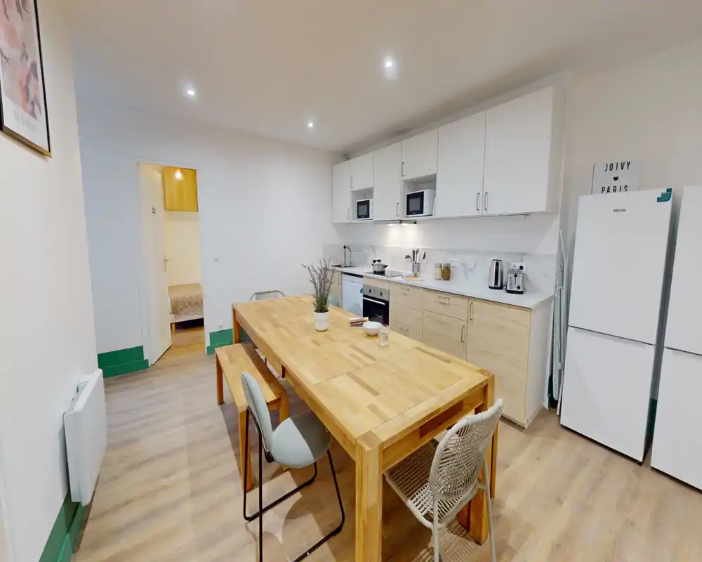 Cuisine moderne ouverte avec une grande table à manger en bois, des meubles intégrés, des appareils électroménagers et un agencement lumineux et soigné — idéal pour cuisiner et partager des repas.