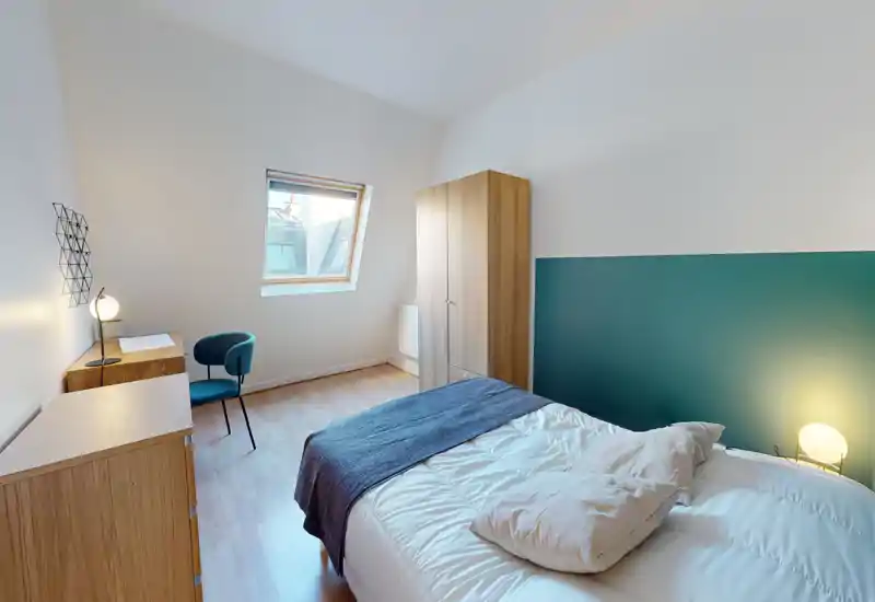 Chambre lumineuse et moderne avec un lit double confortable, un mur d'accent bleu-vert et une fenêtre de toit apportant de la lumière naturelle ; armoire et bureau en bois pour une disposition fonctionnelle.