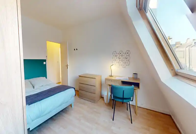 Chambre moderne et lumineuse avec un lit double confortable, sol en bois, petit bureau et grande fenêtre de toit apportant une belle lumière naturelle — idéale pour se reposer ou travailler.