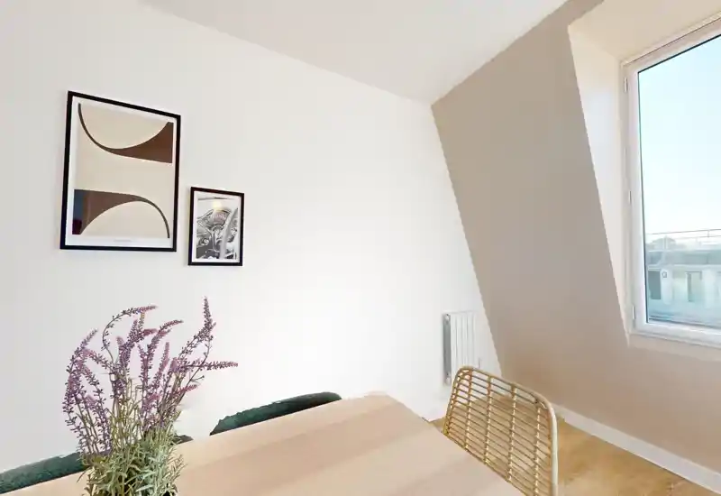 Coin repas lumineux et convivial avec table en bois, chaise tressée et décor mural près d'une fenêtre ensoleillée.