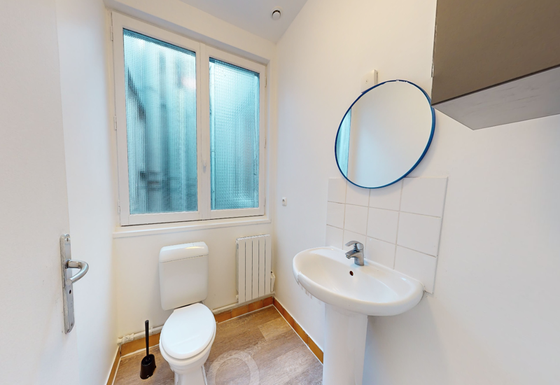 Salle de bain simple et lumineuse avec WC, lavabo sur pied et miroir rond ; fenêtre occultante pour plus d'intimité.