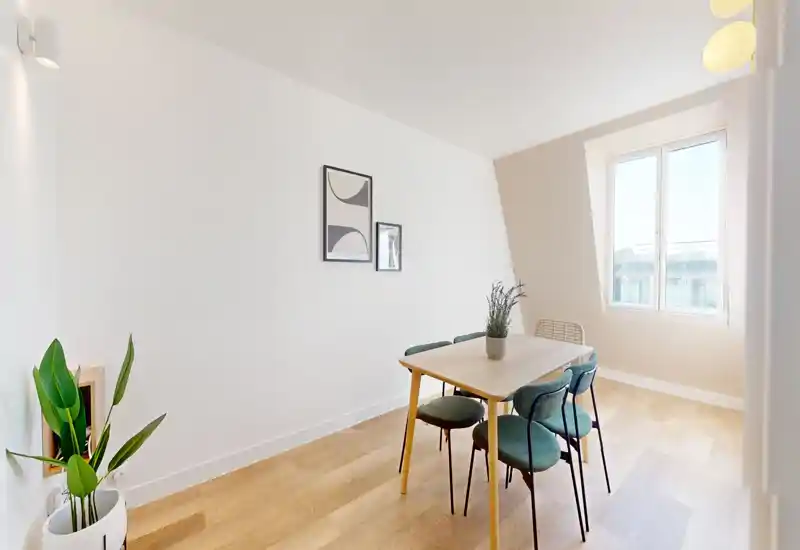 Salle à manger lumineuse et minimaliste avec table en bois, quatre chaises vertes et une grande fenêtre apportant une belle lumière naturelle.