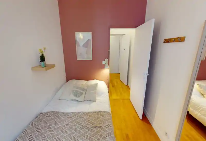 Camera da letto compatta e accogliente con letto singolo contro una parete colorata, lampada da comodino e decorazioni semplici — perfetta per soggiorni brevi.