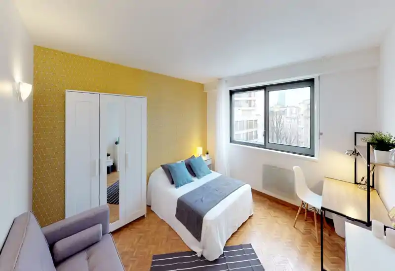 Bright, well-staged bedroom with a double bed dressed in white linen, decorative cushions and a grey runner. Large window provides ample natural light; a desk and wardrobe make the space practical for short or long stays.