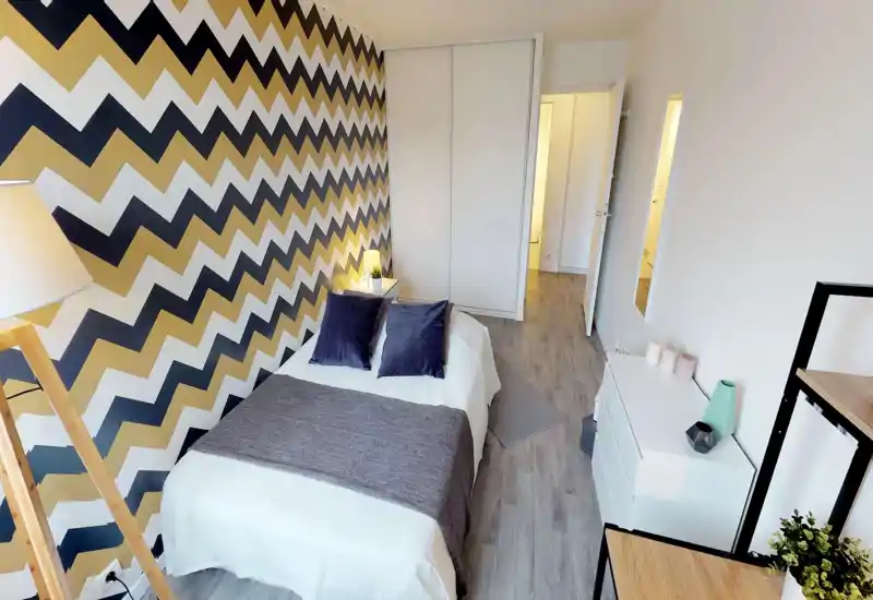 Stylish bedroom with a double bed, decorative pillows, bedside table and a bold chevron-accent wall; bright, well-styled and ready for guests.