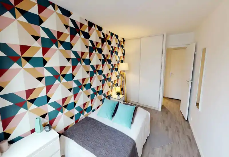 Bright, well-staged bedroom with a double bed, patterned feature wall, bedside table and lamp — a cozy, modern space ideal for restful stays.