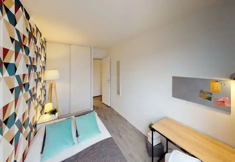 Bright, modern bedroom with a patterned accent wall, a neatly made bed with turquoise cushions, a bedside lamp and a small desk — comfortable and well styled for rental photos.