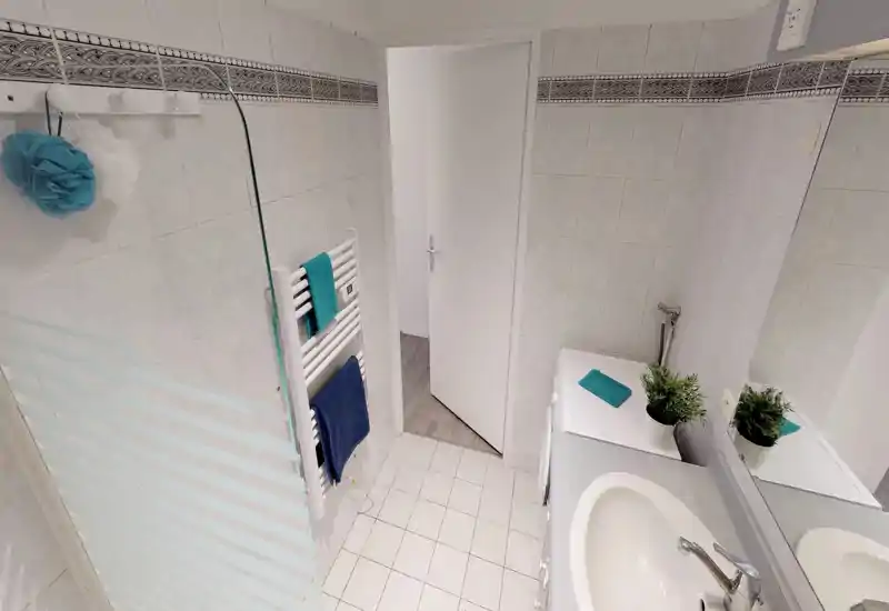 Clean, well-lit bathroom with a sink, mirror, towel radiator and a washing machine surface with plants and neatly placed towels.