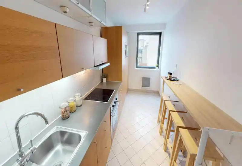 Bright, modern galley kitchen with wooden cabinets, stainless sink and a breakfast bar with stools — ideal for compact urban apartments.