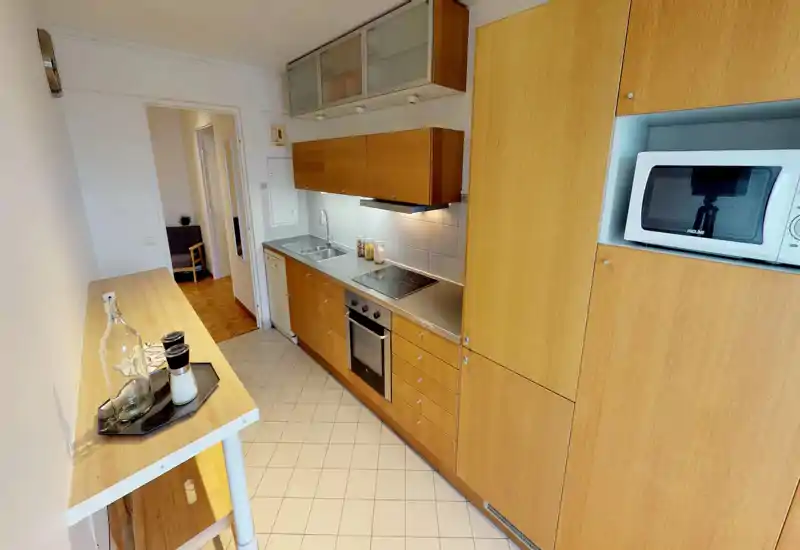 Well-equipped galley kitchen with wooden cabinets, built-in oven and stovetop, microwave and a small breakfast bar — bright and neatly staged for rentals.