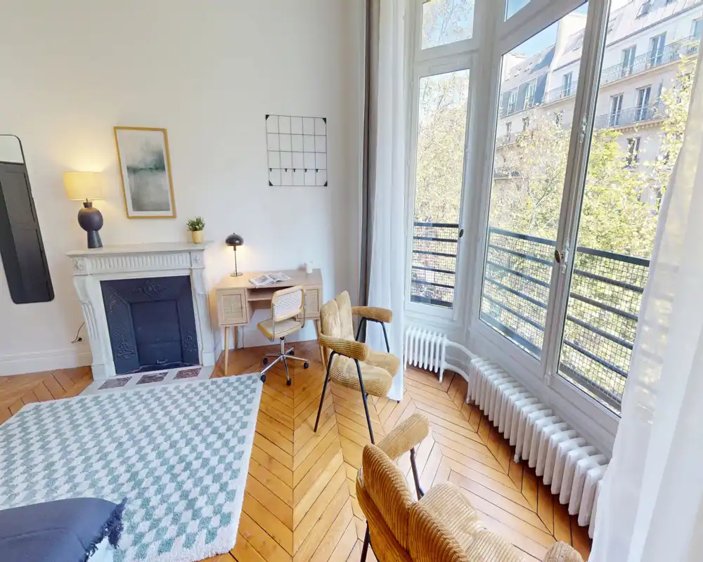 Espace de vie lumineux et stylé avec grandes fenêtres, parquet en chevrons, fauteuils confortables et cheminée décorative — parfait pour se détendre ou travailler.