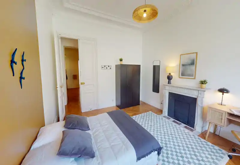 Chambre lumineuse et élégante avec un lit double confortable, tapis à motif et cheminée décorative. Plafonds hauts, parquet et éclairage soigné procurent une atmosphère chaleureuse.