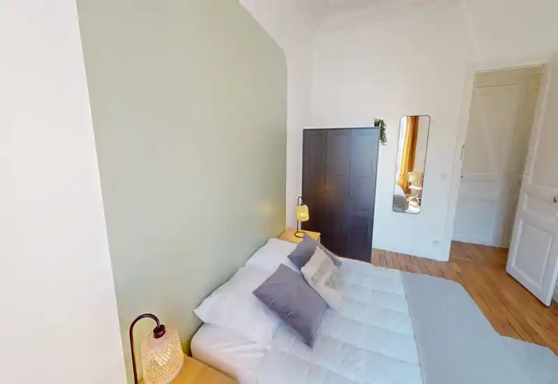 Chambre lumineuse et soignée avec un lit double confortable devant un mur vert doux, lampes de chevet et armoire — chaleureuse et bien éclairée pour une annonce.