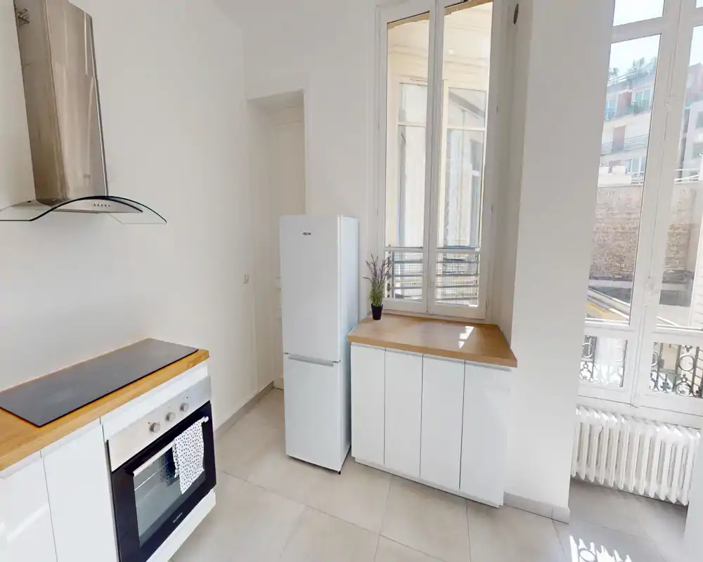 Cuisine moderne et lumineuse avec placards blancs, plans de travail en bois, four encastré et grandes fenêtres offrant une belle lumière naturelle.