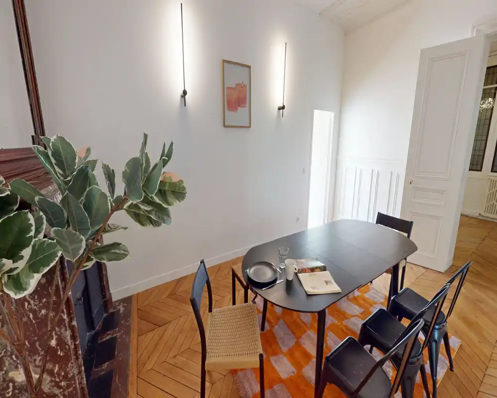 Salle à manger élégante avec une table noire moderne, des chaises variées et un sol en parquet point de Hongrie réchauffé par un tapis coloré ; bien éclairée et décorée avec goût pour des repas conviviaux.