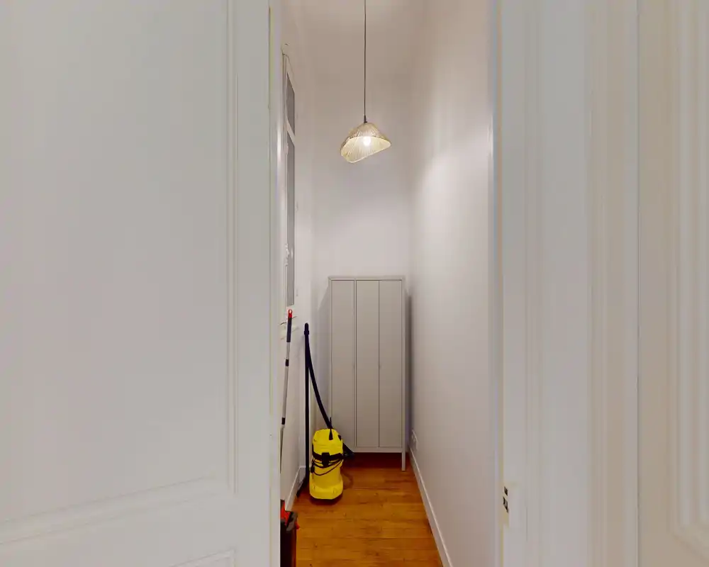 Entrée/couloir étroit avec sol en bois, une armoire de rangement et un aspirateur — zone d'entrée utilitaire et fonctionnelle.