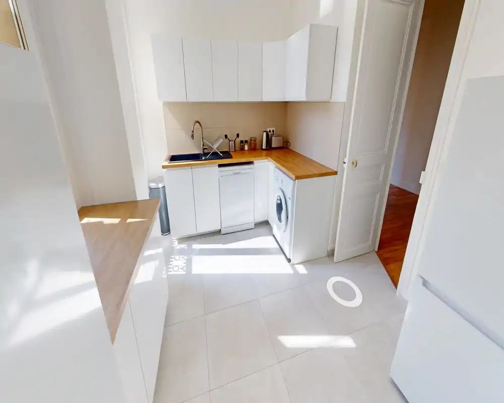 Cuisine moderne et lumineuse avec placards blancs, plans de travail en bois, évier intégré, lave-vaisselle et lave-linge ; design minimaliste et lumineux.