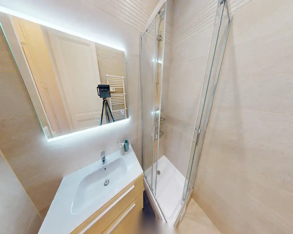 Salle de bain moderne et compacte avec cabine de douche en verre, miroir éclairé et vasque avec meuble — lumineuse, propre et bien finie.