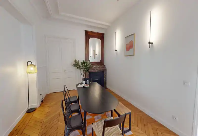 Bright, elegant dining room with a long black dining table, mixed chairs, decorative rug and a classic fireplace with mirror — ideal for dinners and meetings.