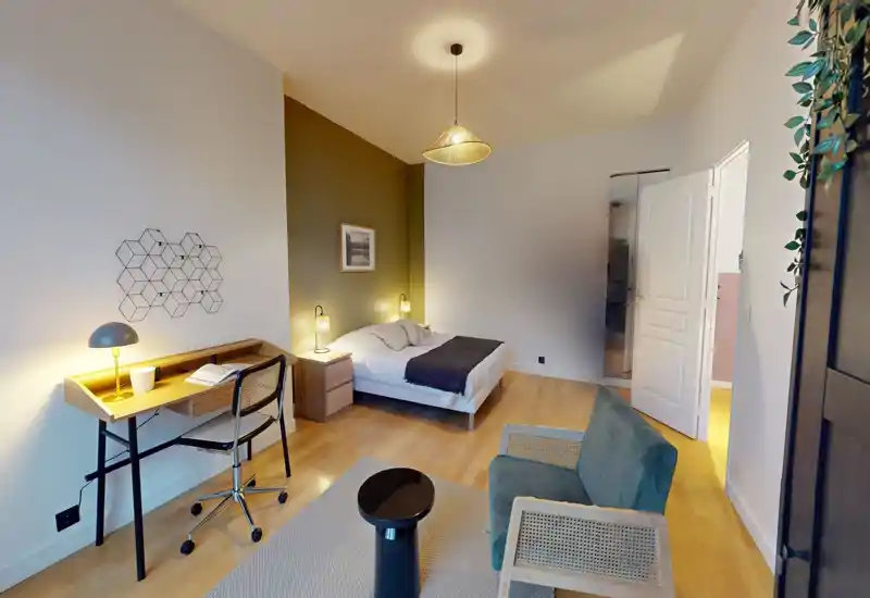 Chambre lumineuse et élégante avec lit double, tables de chevet et éclairage chaleureux ; bureau et coin salon confortable pour un séjour agréable.