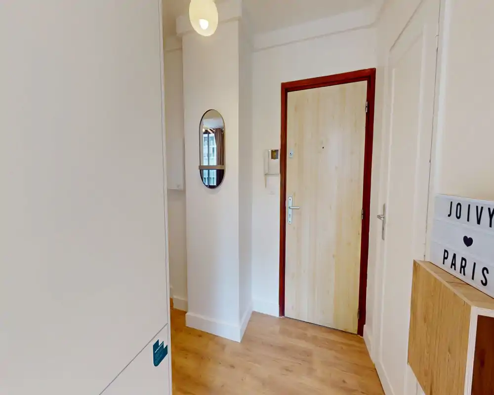 Bright, minimal apartment entrance with a wooden floor, a light-colored door, a small mirror on the wall and tidy storage, offering a welcoming first impression.