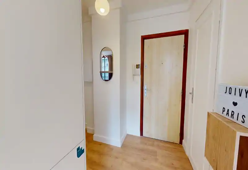 Bright, minimal apartment entrance with a wooden floor, a light-colored door, a small mirror on the wall and tidy storage, offering a welcoming first impression.