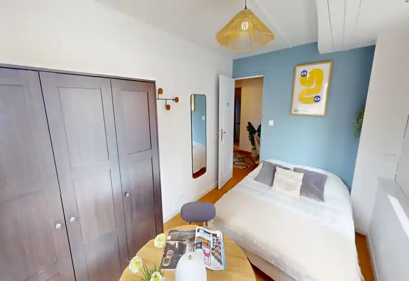 Dormitorio acogedor y amueblado con cama doble, cojines decorativos, cuadro en la pared y armario. La luz natural y los tonos suaves crean un ambiente cálido y atractivo para un anuncio de alquiler.