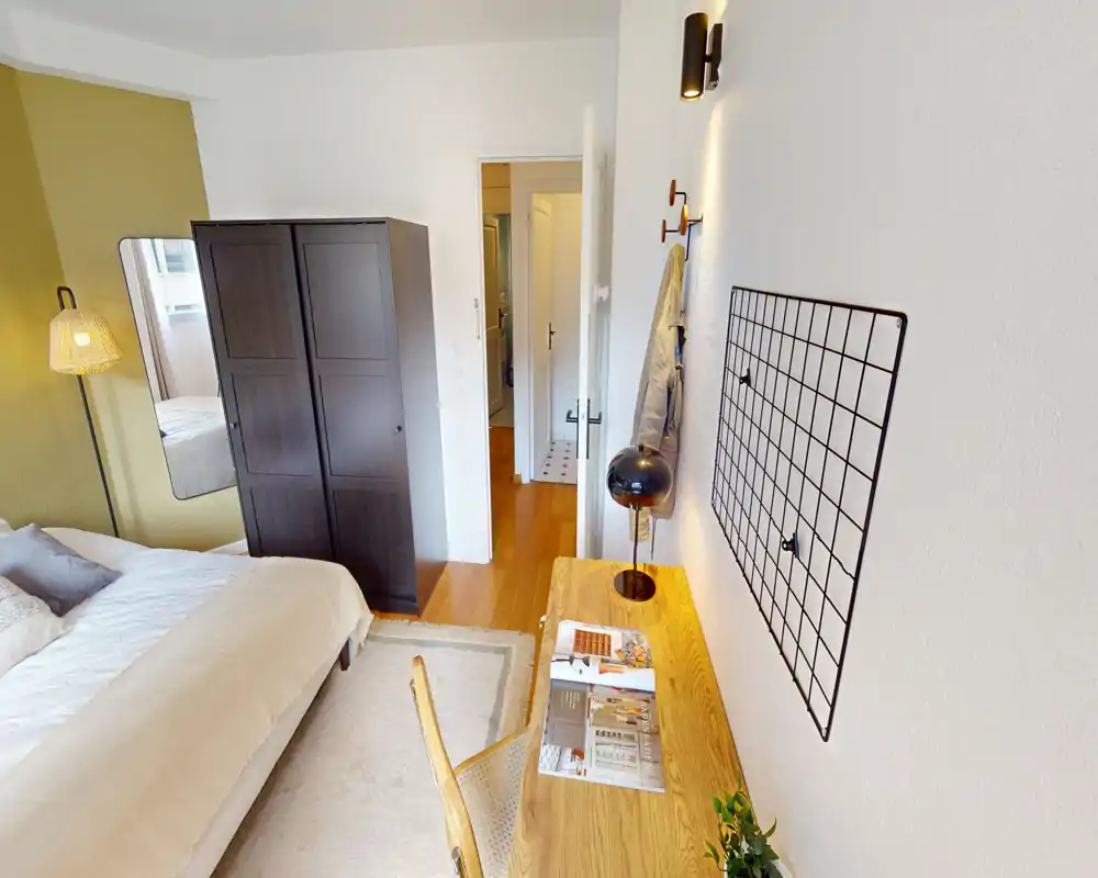 Camera da letto luminosa e ben arredata con un comodo letto matrimoniale, armadio e scrivania in legno; l'illuminazione calda e i toni neutri creano un'atmosfera accogliente.