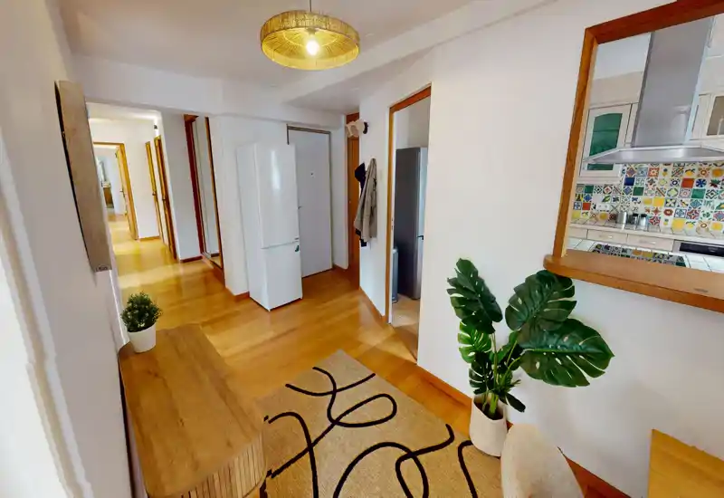 Entrée lumineuse et accueillante avec sol en bois, tapis décoratif et vue sur la cuisine via une ouverture de service.