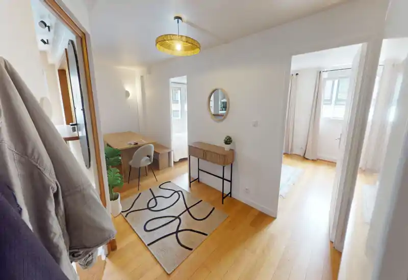 Entrée lumineuse et accueillante avec parquet, console et miroir rond décoratif — desservant les pièces adjacentes et un petit coin bureau.