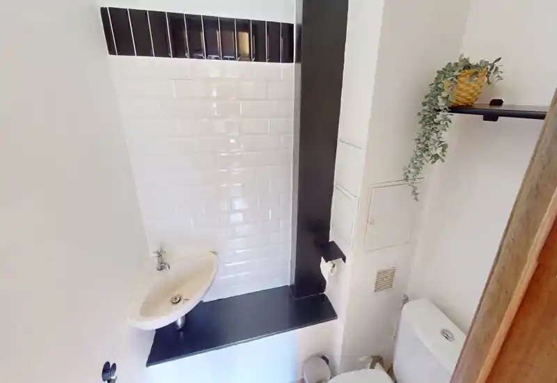 Salle de bain compacte et lumineuse avec carreaux métro blancs, petit lavabo mural et WC — style minimaliste et propre, parfait pour une location courte durée.