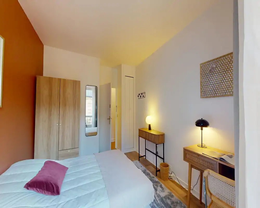 Chambre lumineuse et chaleureuse avec lit double, tables et lampes de chevet, armoire et petit espace de travail — idéale pour un séjour confortable.