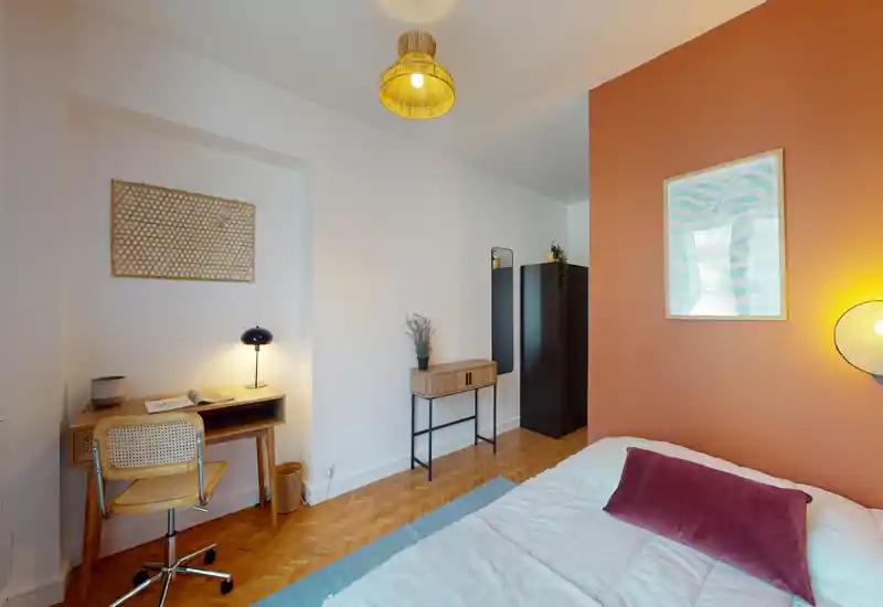 Chambre lumineuse et élégante avec un lit confortable, un mur d'accent chaleureux et des lampes d'appoint. Un petit bureau et une chaise forment un coin travail; textures naturelles et textiles doux donnent une ambiance cosy.