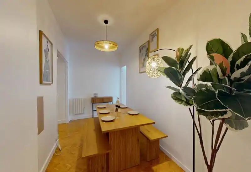 Salle à manger chaleureuse et minimaliste avec table et bancs en bois pour quatre personnes, suspensions lumineuses et plantes décoratives.