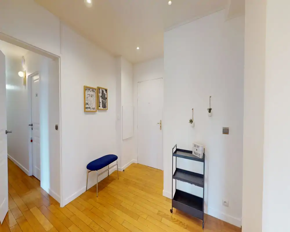 Entrée lumineuse et soignée avec parquet en bois, un petit banc bleu et une étagère chariot noire fine — décoration minimale et belle lumière ambiante.