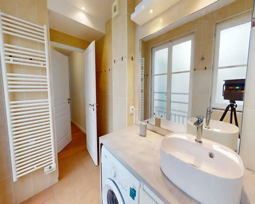 Salle de bains moderne avec vasque posée, grand miroir et fenêtre dépoli ; carrelage mural et sèche-serviettes offrent un espace propre et lumineux.