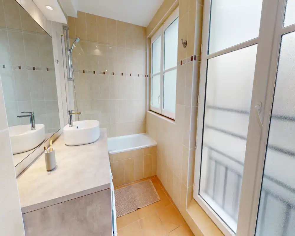 Salle de bains lumineuse et bien éclairée avec baignoire, lavabo moderne et grande fenêtre dépoli offrant intimité et lumière naturelle.