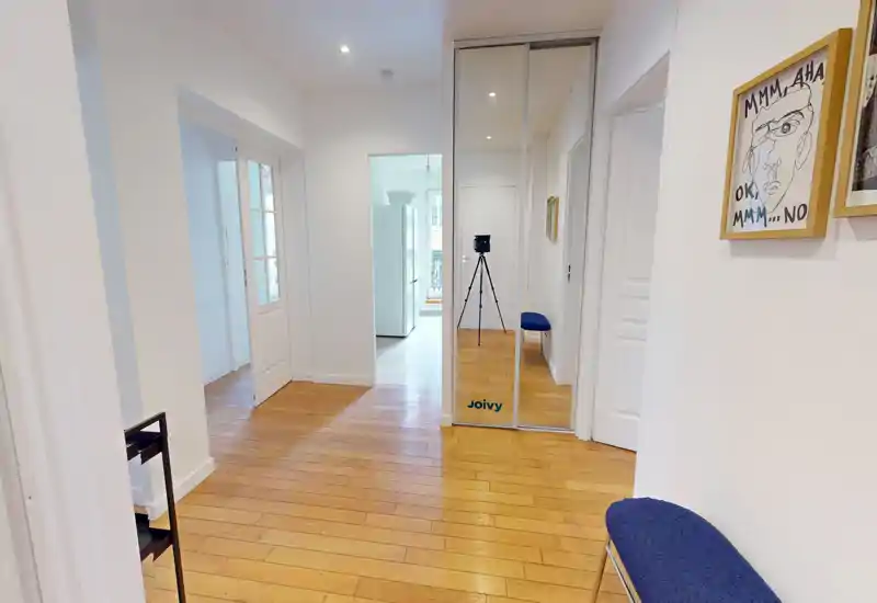 Bright, clean entrance hall with wooden flooring, mirrored closet doors and a small bench — a welcoming arrival area with clear sightlines into adjacent rooms.